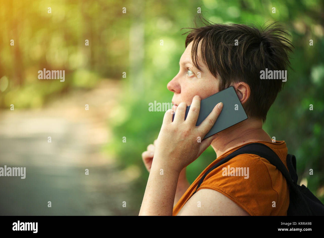 Woman talking on mobile phone in park, femelle adulte backpacker la marche à l'extérieur et l'utilisation de smartphone pour la communication. Banque D'Images