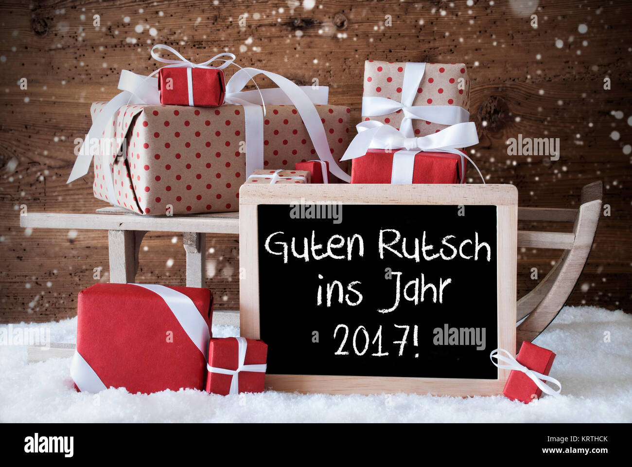 Tableau sur lequel un texte Allemand Guten Rutsch ins Jahr 2017 signifie bonne année. Traîneau avec Noël et la décoration de l'hiver et les flocons de neige. Cadeaux et présente sur la neige en fond de bois. Banque D'Images