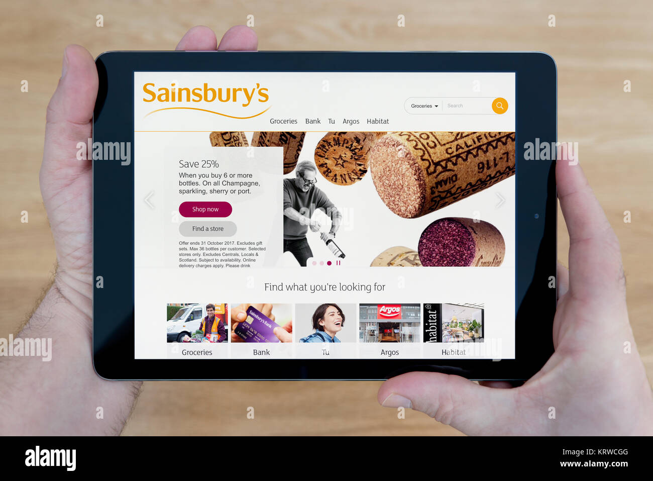 Un homme regarde le supermarché Sainsbury's site sur son iPad tablet device, tourné contre une table en bois page contexte (usage éditorial uniquement) Banque D'Images