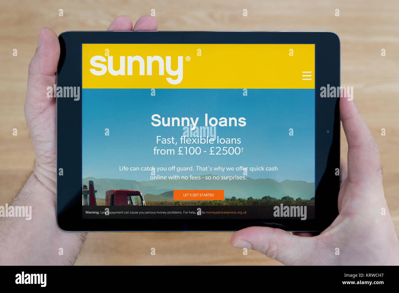 Un homme regarde le soleil de prêts sur salaire site sur son iPad tablet device, tourné contre une table en bois page contexte (usage éditorial uniquement) Banque D'Images