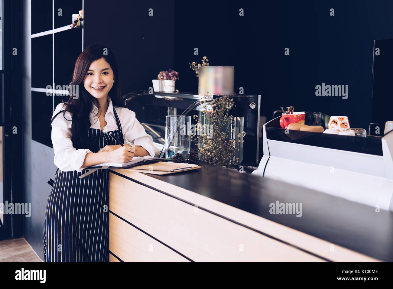 Propriétaire de petite entreprise avec compteur à l'ordinateur portable dans un café. asian female barista portant un tablier écrit remarque au bar en café, restaurant service alimentaire. Banque D'Images