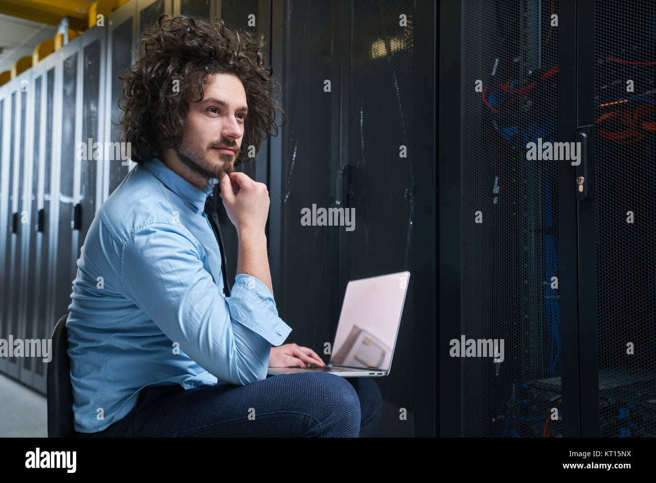 Jeune technicien travaillant sur un ordinateur portable à côté de racks de serveur noir Banque D'Images