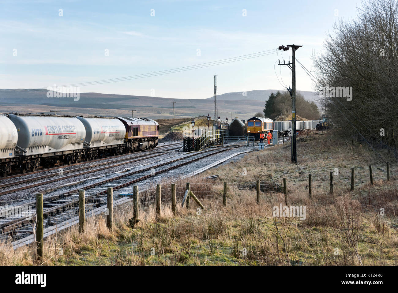 Cement wagon train tiré par une locomotive Classe 66 Chargement d'un autre train passe dans le parement en pierre à Ribblehead Station, North Yorkshire, UK Banque D'Images