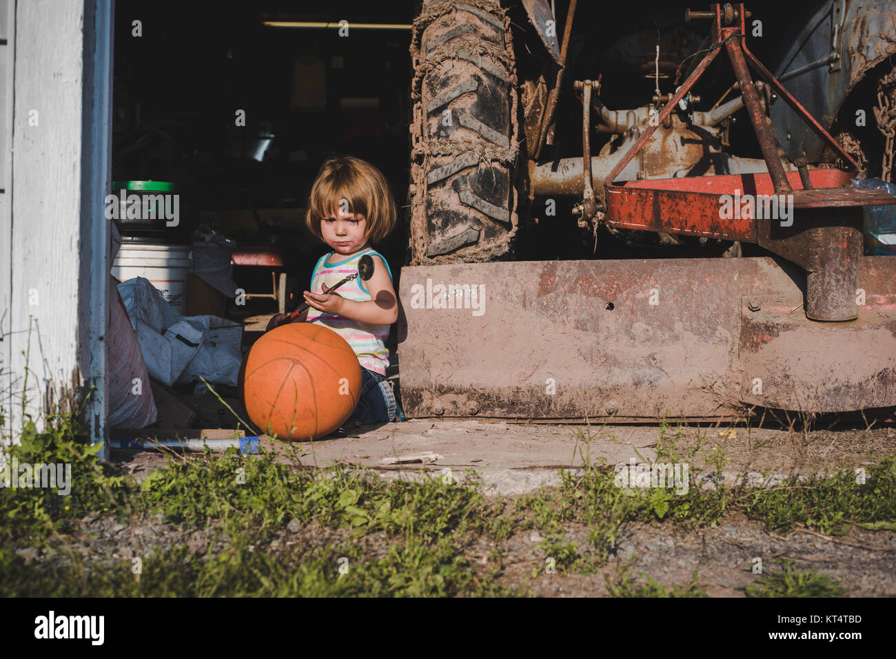 Une petite fille est assise à côté d'un tracteur et d'une antique de  basket-ball orange dans une porte de garage Photo Stock - Alamy