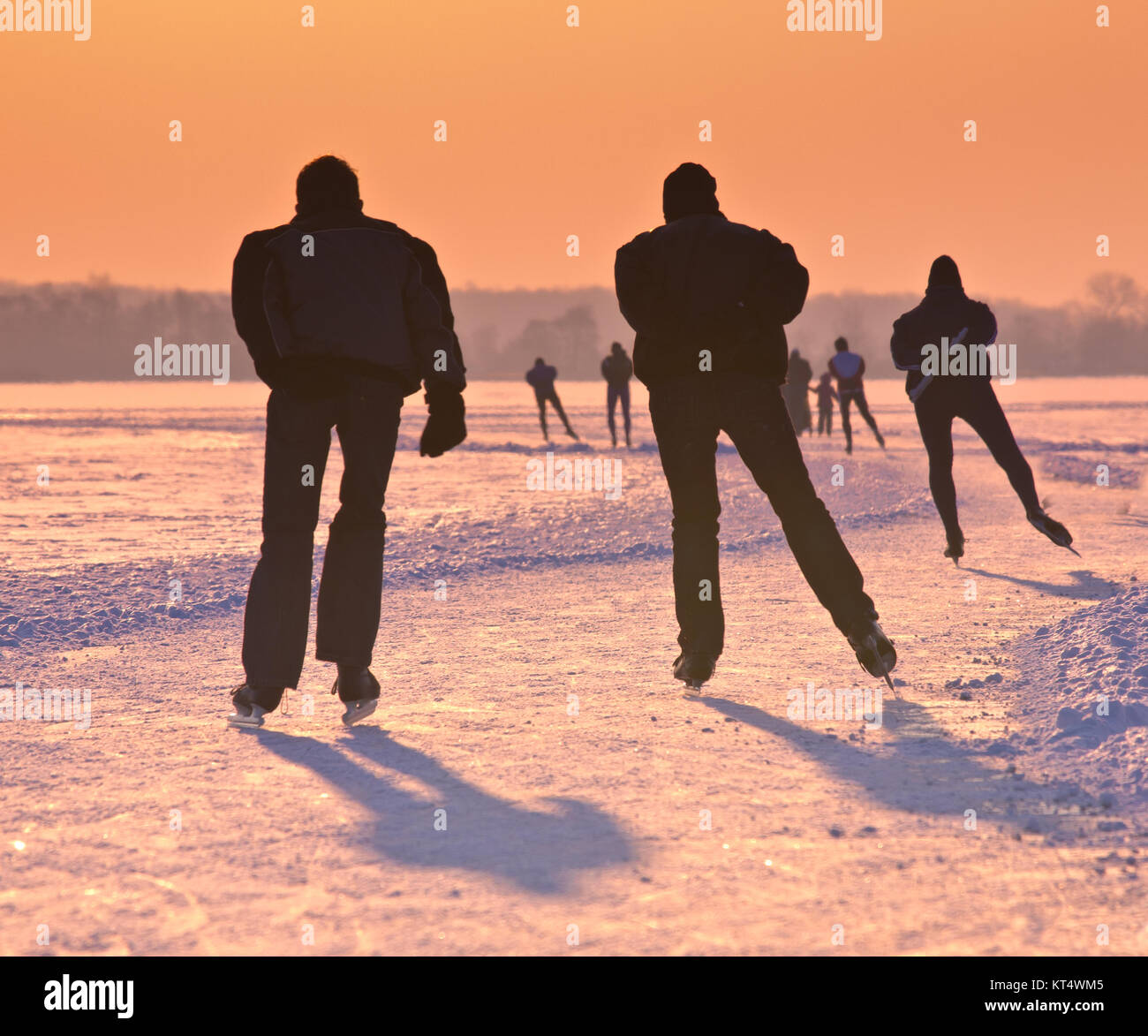 Patineurs sur un lac gelé vu sur leur dos sous beau coucher du soleil Banque D'Images