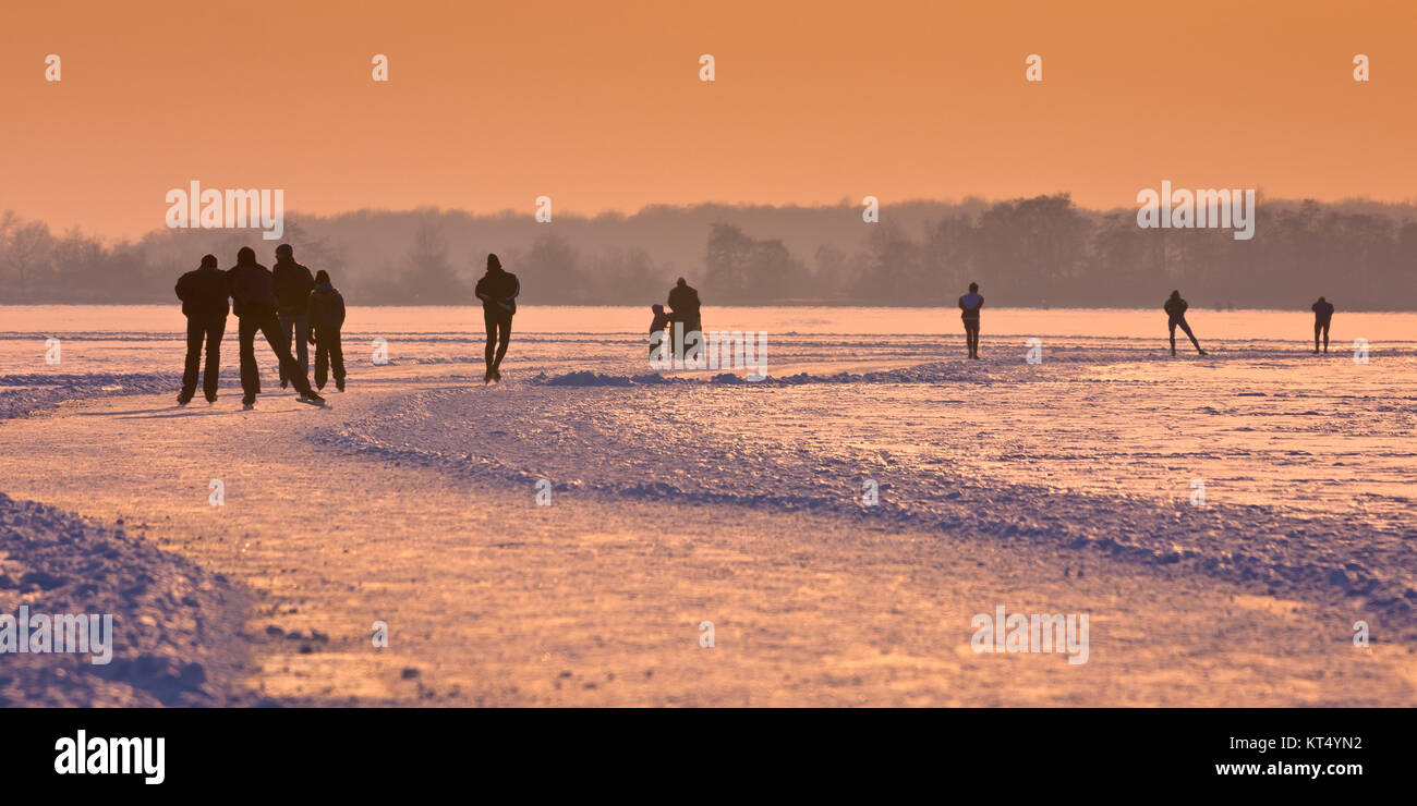 Patineurs sur un lac gelé vu sur leur dos sous coucher du soleil orange Banque D'Images