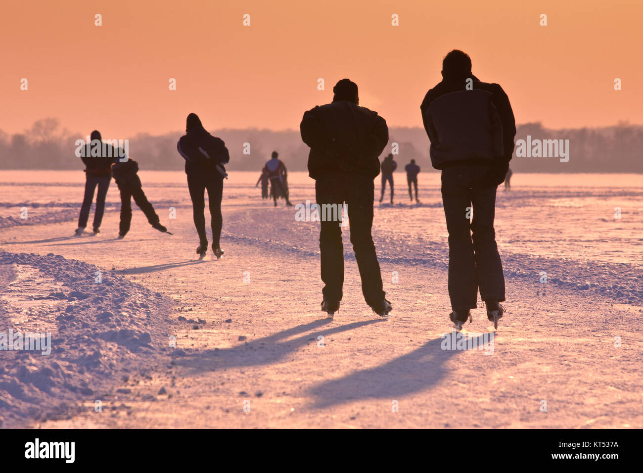 Patineurs sur un lac gelé vu sur leur dos sous coucher du soleil orange Banque D'Images