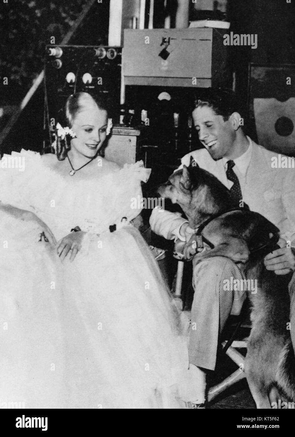 Rudy Vallée, un chanteur américain populaire, est vu ici avec l'actrice Gloria Stuart et un chien policier. Cette photographie capture un moment de célébrité et d'histoire culturelle au début du XXe siècle, mettant en valeur le charme des deux étoiles. Banque D'Images