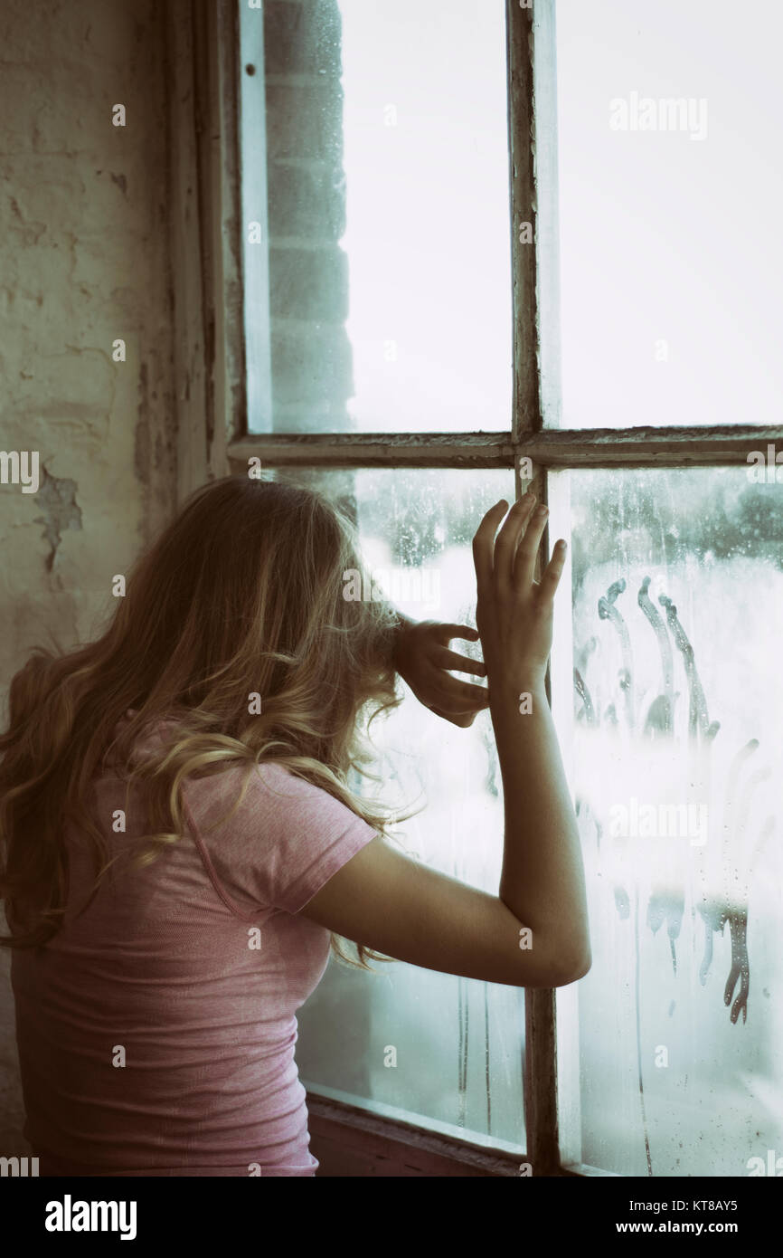 Vue arrière d'une femme blonde debout près de la fenêtre les mains de toucher le verre Banque D'Images