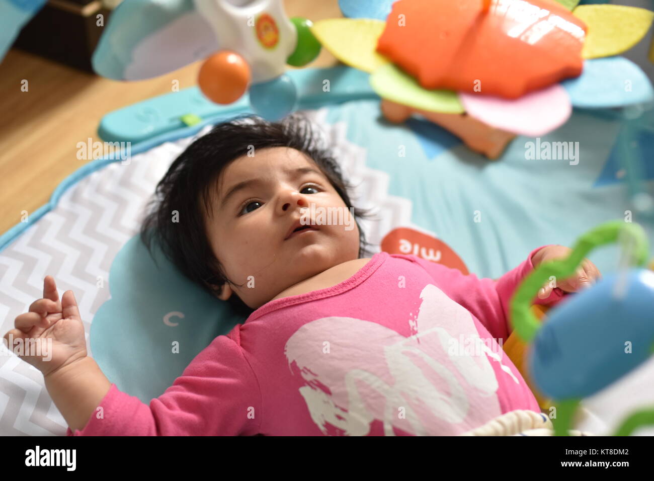 Bébé curieux girl examine la pendaison des jouets de son tapis de jeu avec beaucoup d'attention Banque D'Images