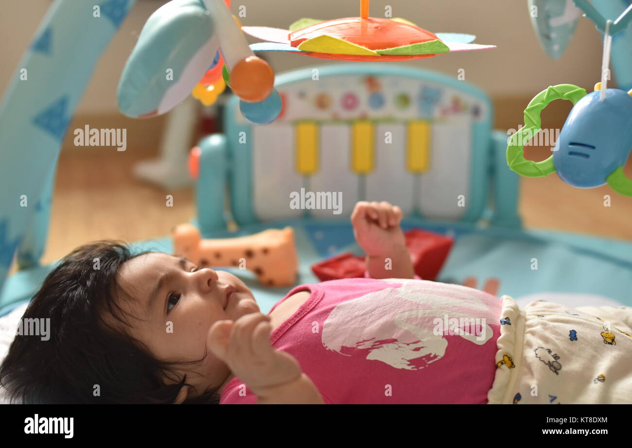 Baby Girl observe attentivement ses jouets suspendus à partir de son tapis de jeu Banque D'Images