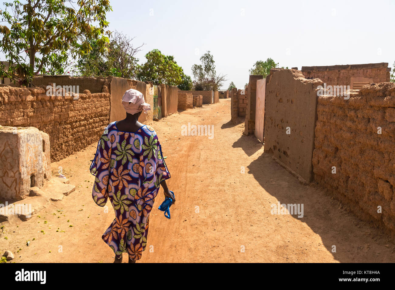 Une femme marche avec des vêtements colorés et traditionnels dans un taudis street dans la banlieue de Ouagadougou, Burkina Faso, Afrique de l'Ouest. Banque D'Images