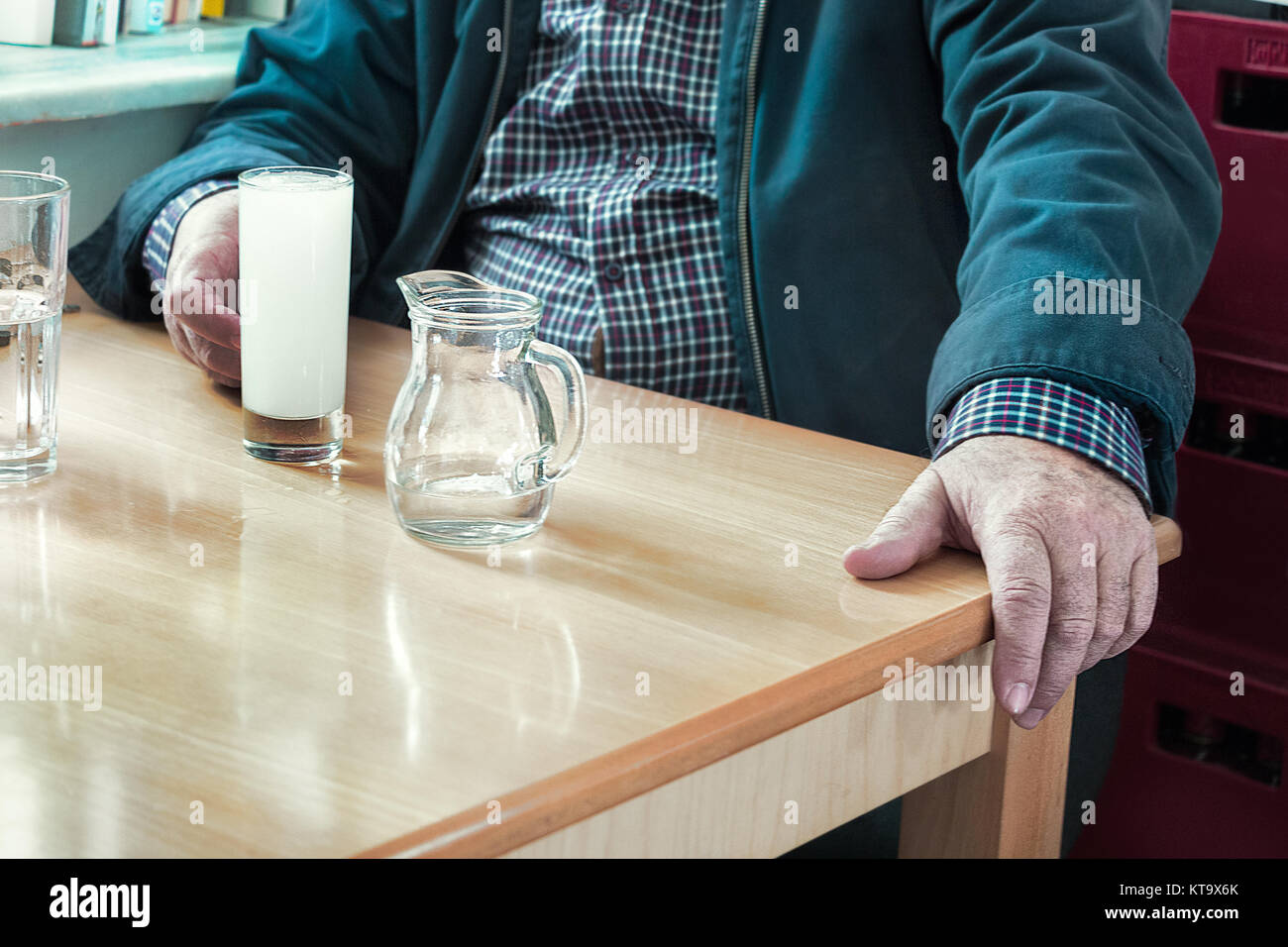 Un homme assis avec sa main sur une table et un verre d'ouzo et un pot d'eau à l'intérieur d'une taverne grecque ouzeri traditionnels. Banque D'Images