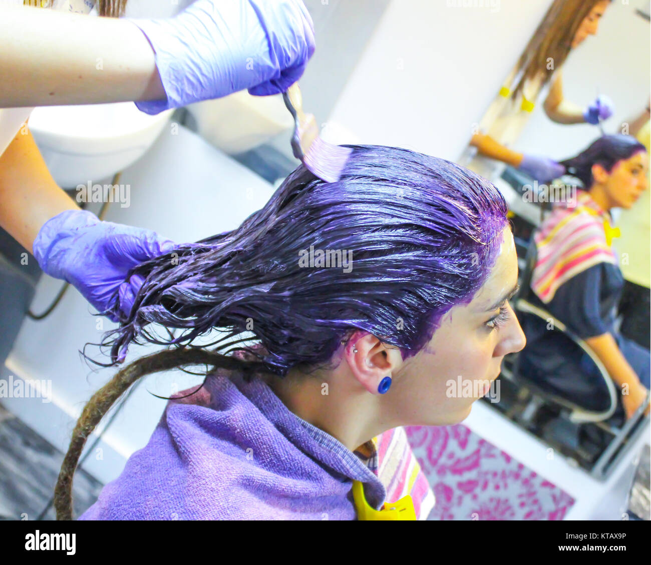 Jeune femme cheveux coloration lilas dans le salon de coiffure à l'aide d'une serviette. Elle a une longue tresse rasta c'est ; non peinte est assis en face du miroir Banque D'Images