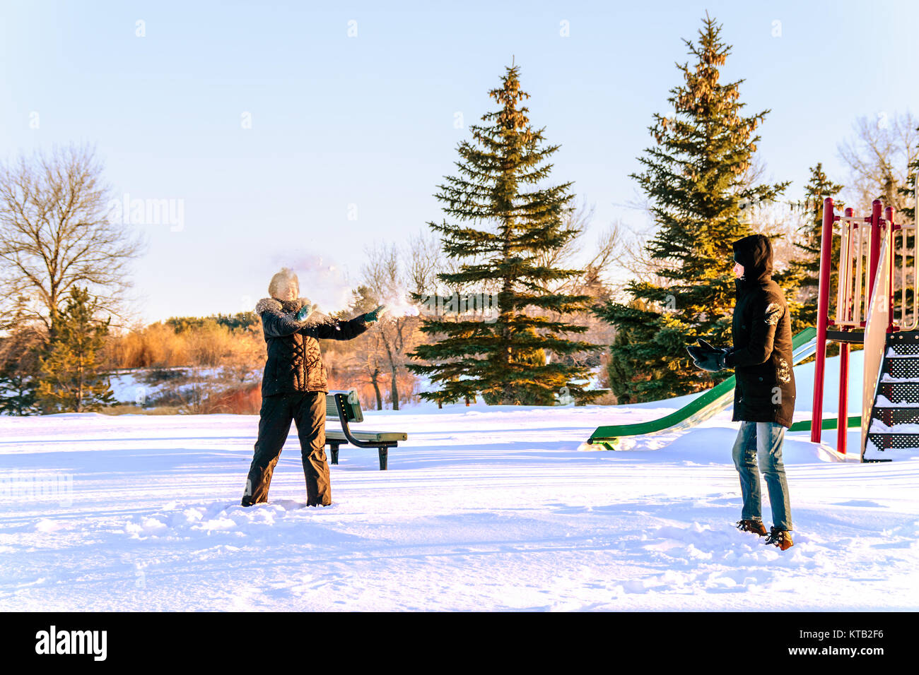 Au premier plan, une jeune femme en combinaisons noires lunettes dans un établissement 3 étoiles avec joie et lance une boule de neige à un jeune homme dans une veste noire et un jean. Banque D'Images