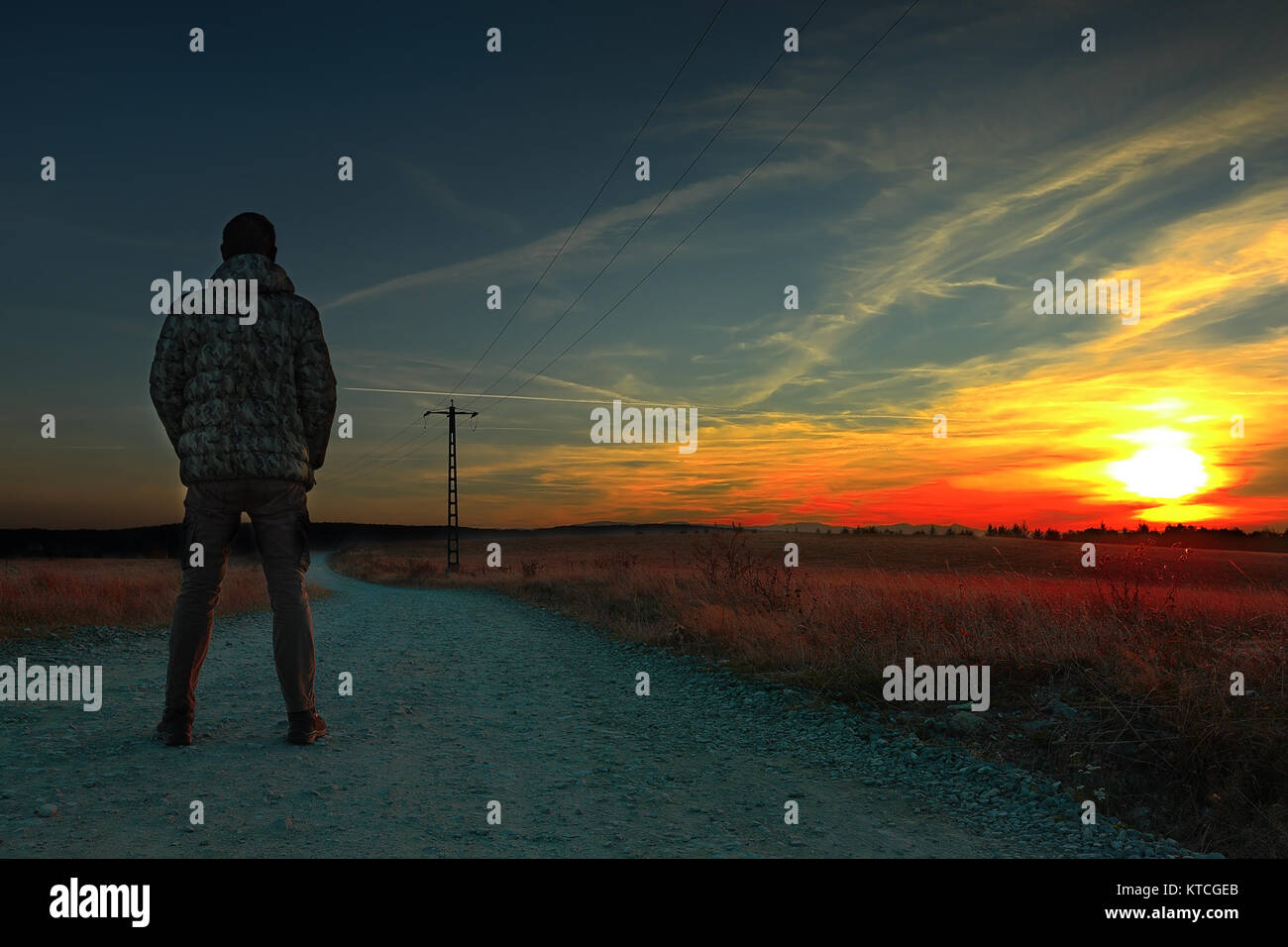 L'homme regardant le coucher de soleil colorés de rural road Banque D'Images