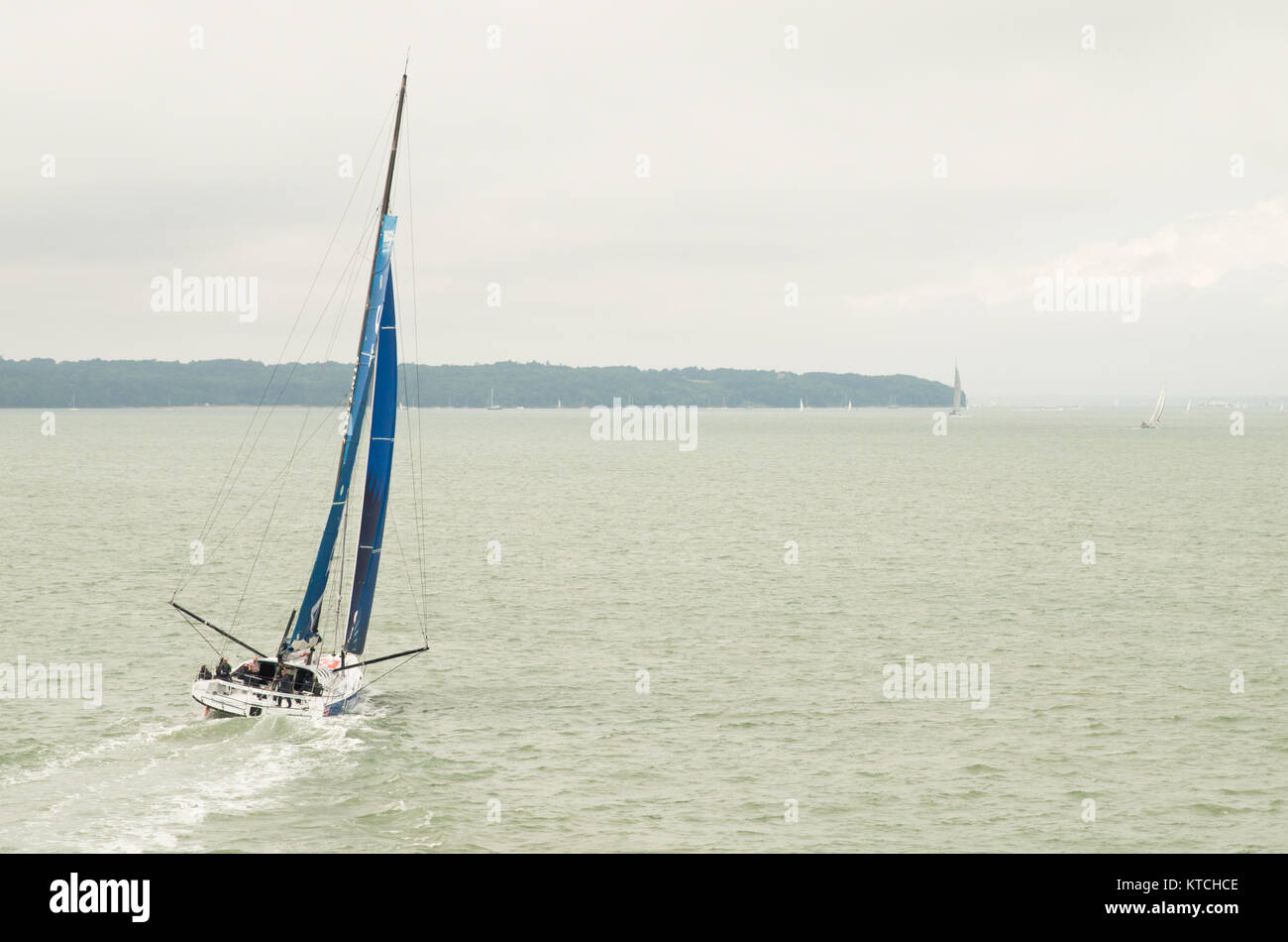Un yacht à voile bleu sur le Solent avec l'île de Wight dans la distance. Banque D'Images