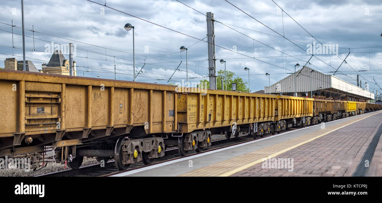 Train de marchandises avec wagons-trémies jaunes sur le quai de la gare ferroviaire sous un ciel nuageux. Banque D'Images