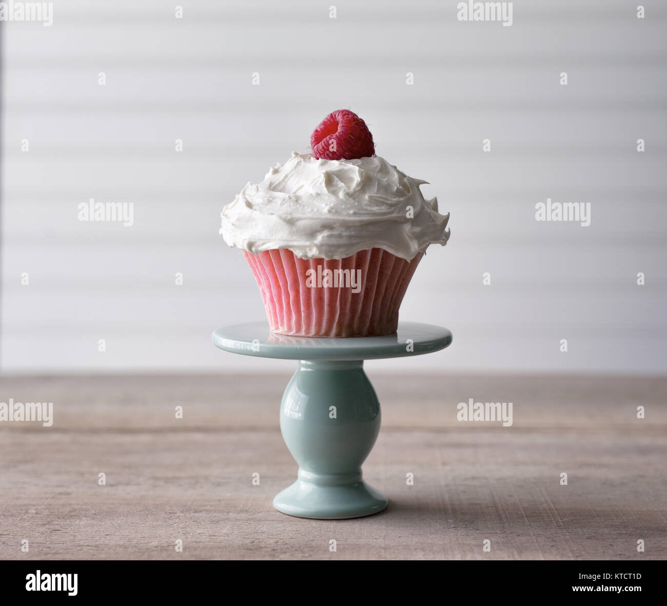 Cupcake rose avec garniture framboises fraîches servies à partir d'un mini plat à gâteau. Sur un fond blanc. Copier l'espace. Banque D'Images