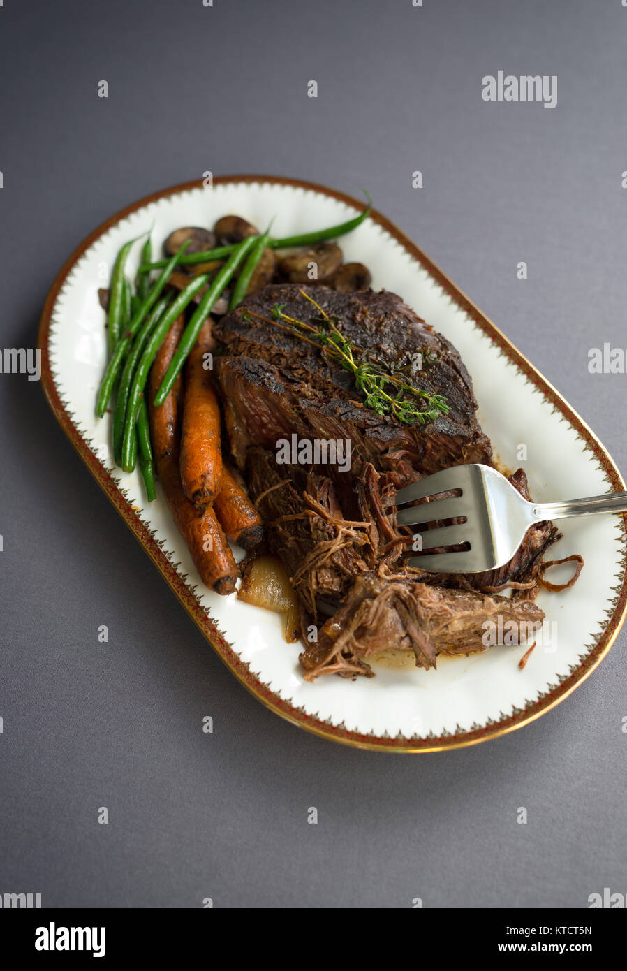 De mijotés avec les haricots verts, les carottes et les champignons sur une assiette blanche. Nappe grise, garnir de thym. Copier l'espace. Banque D'Images