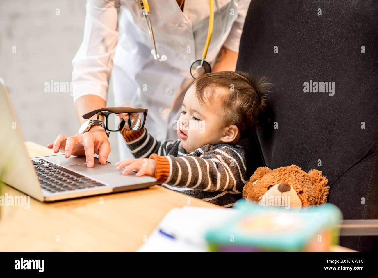 L'examen de l'infirmière de santé d'un bébé garçon jouant sur l'ordinateur portable dans le bureau Banque D'Images