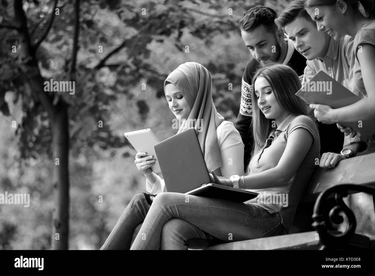 Groupe de jeunes à l'aide d'ordinateur portable et tablette sur un banc de parc, s'amuser, parler, sortir Banque D'Images