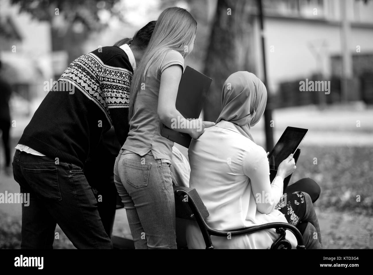 Groupe de jeunes à l'aide d'ordinateur portable et tablette sur un banc de parc, s'amuser, parler, sortir Banque D'Images