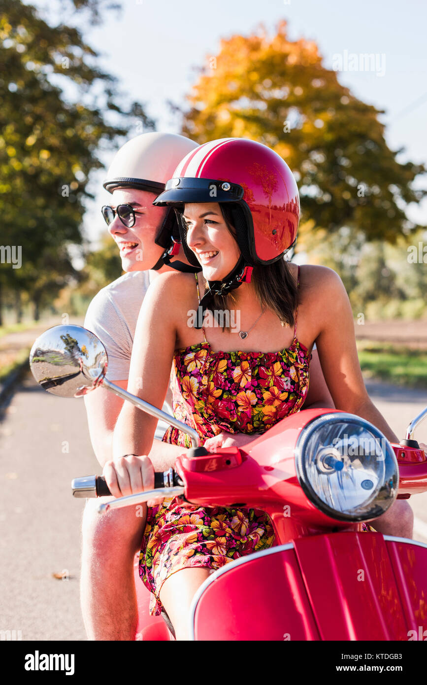 Happy young couple riding scooter on country road Banque D'Images