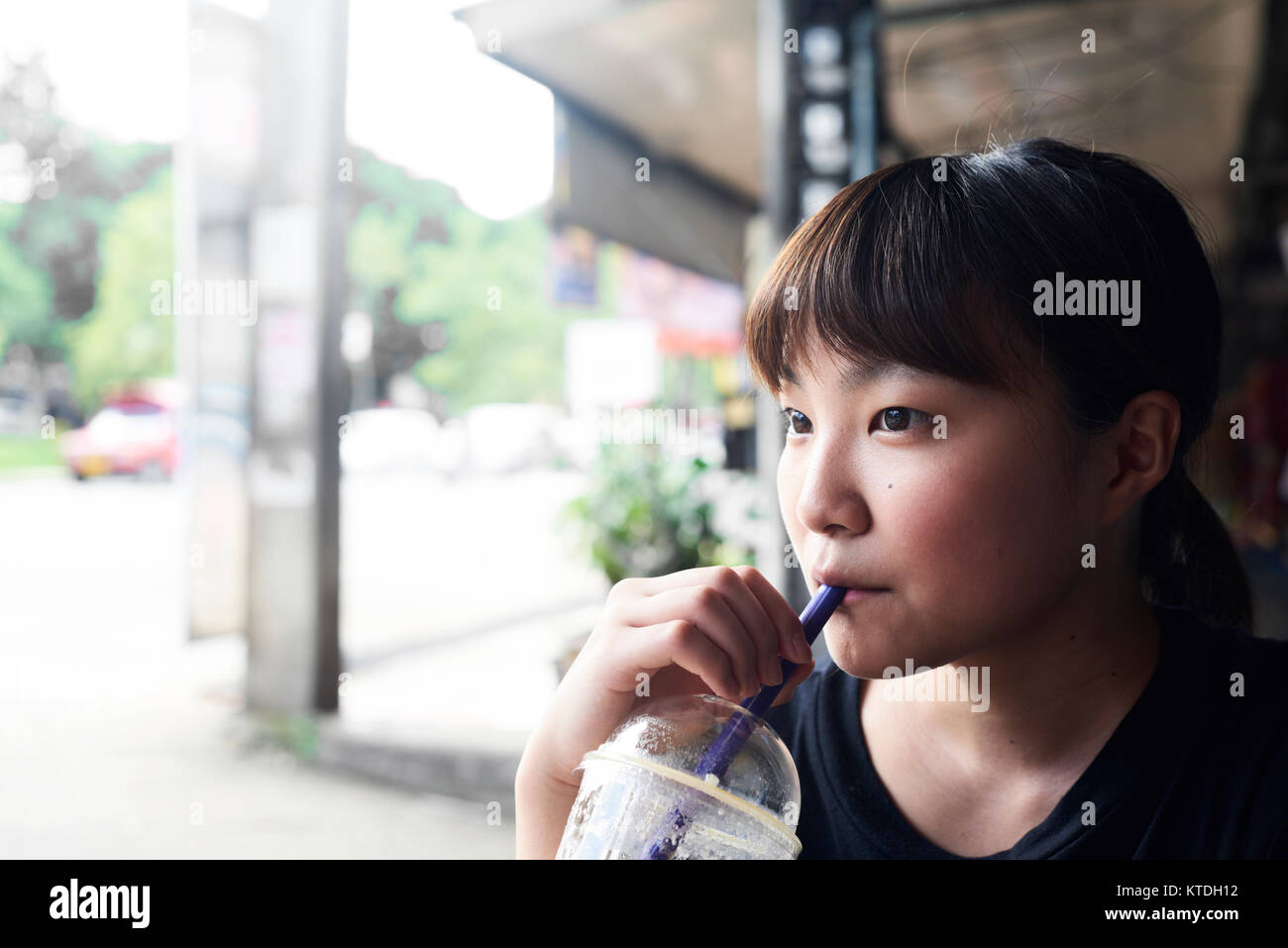 Jolie femme d'origine asiatique de boire un smoothie tout en thiking dans un environnement urbain. Chiang Mai, Thaïlande. Banque D'Images