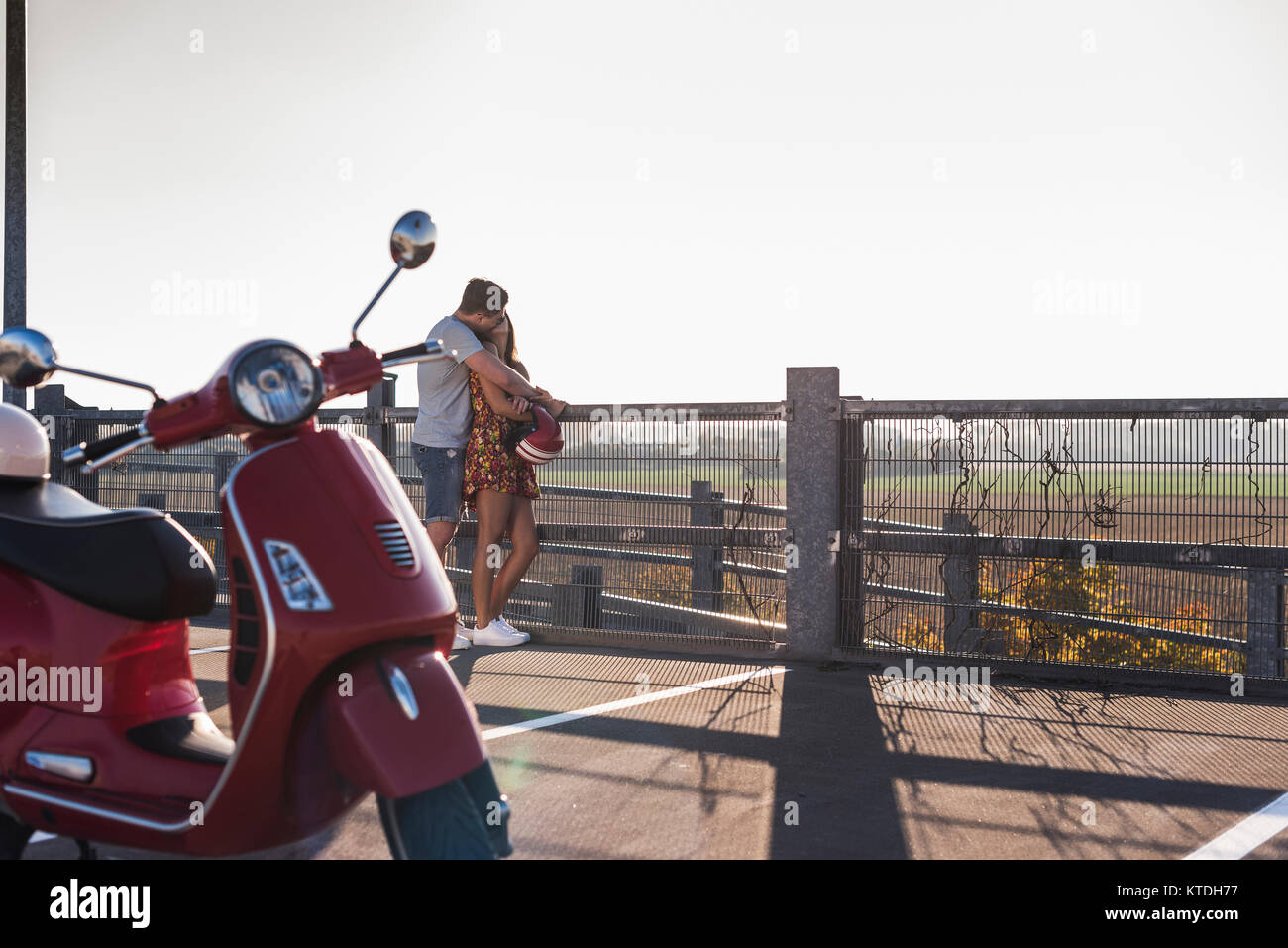 Couple sur parking avec scooter en premier plan Banque D'Images