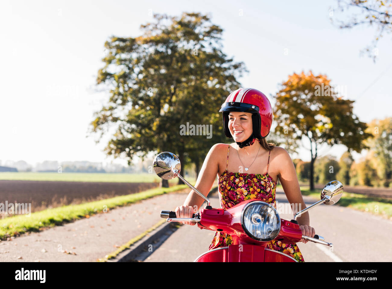 Happy young woman riding scooter on country road Banque D'Images