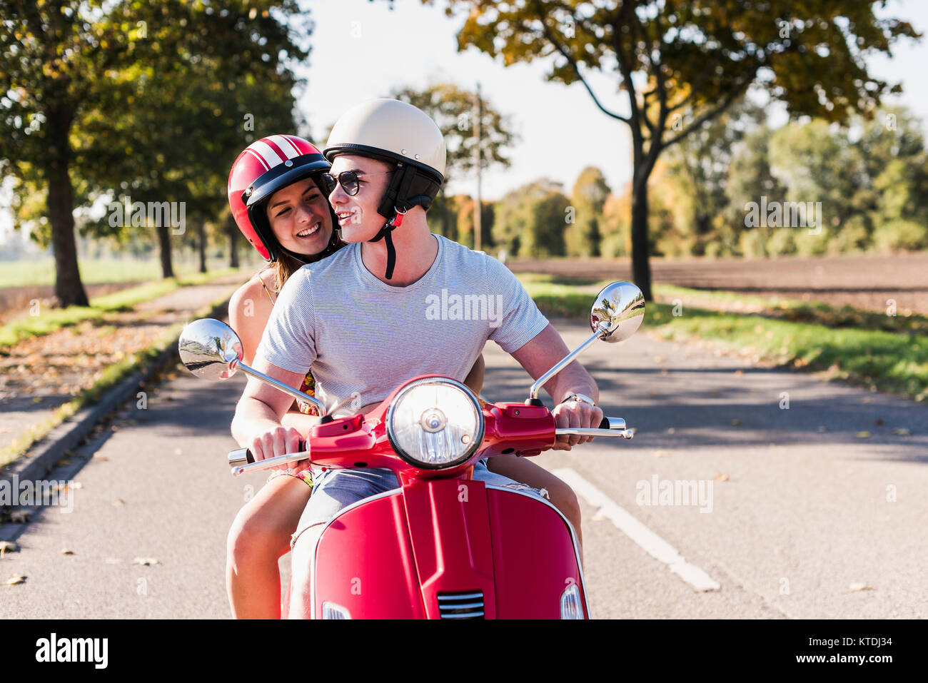 Happy young couple riding scooter on country road Banque D'Images