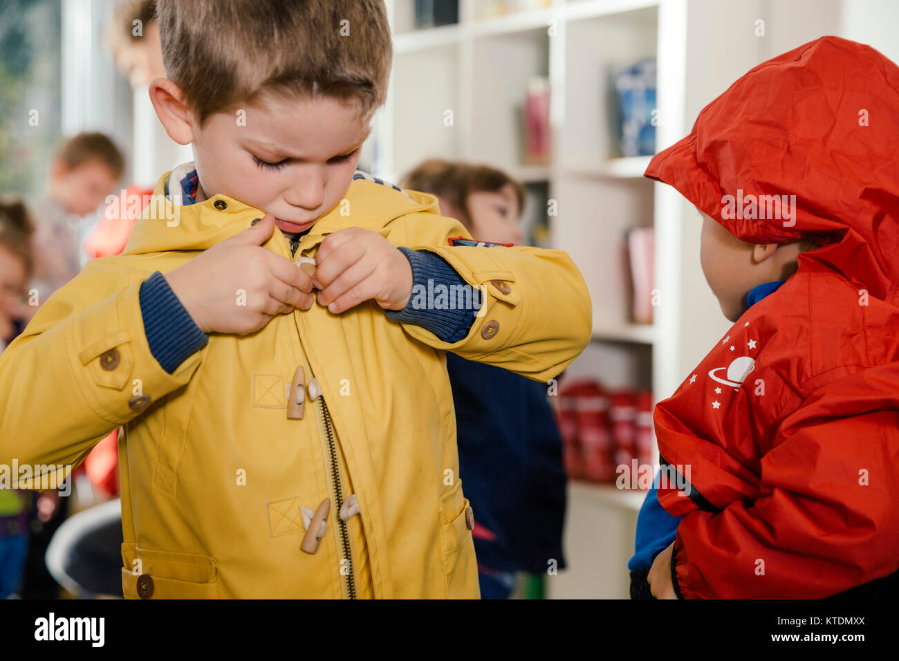 Boy putting sur son imperméable à la maternelle Banque D'Images