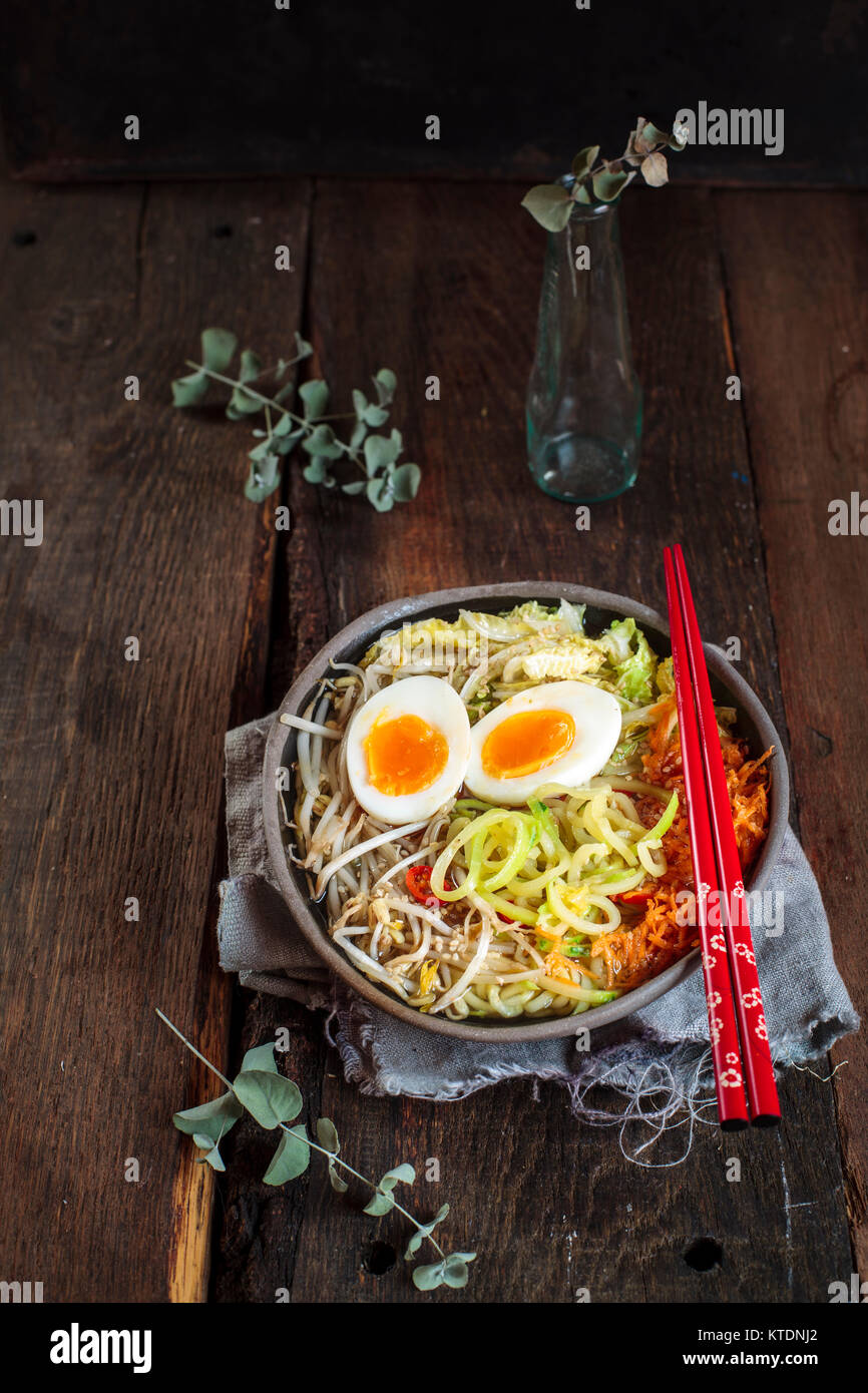 Bol de soupe de nouilles Udon sans gluten avec des carottes, chou chinois, germes de haricots mungo, zoodles et oeuf dur Banque D'Images