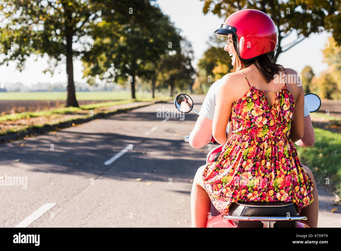 Happy young couple riding scooter on country road Banque D'Images