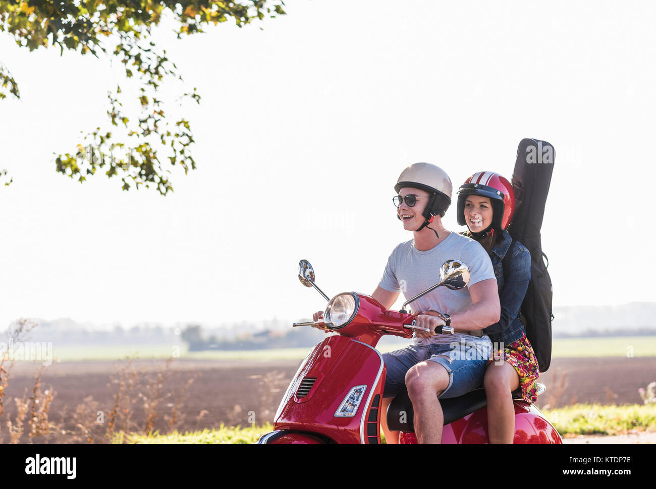 Happy young couple riding scooter avec guitare sac sur le dos Banque D'Images