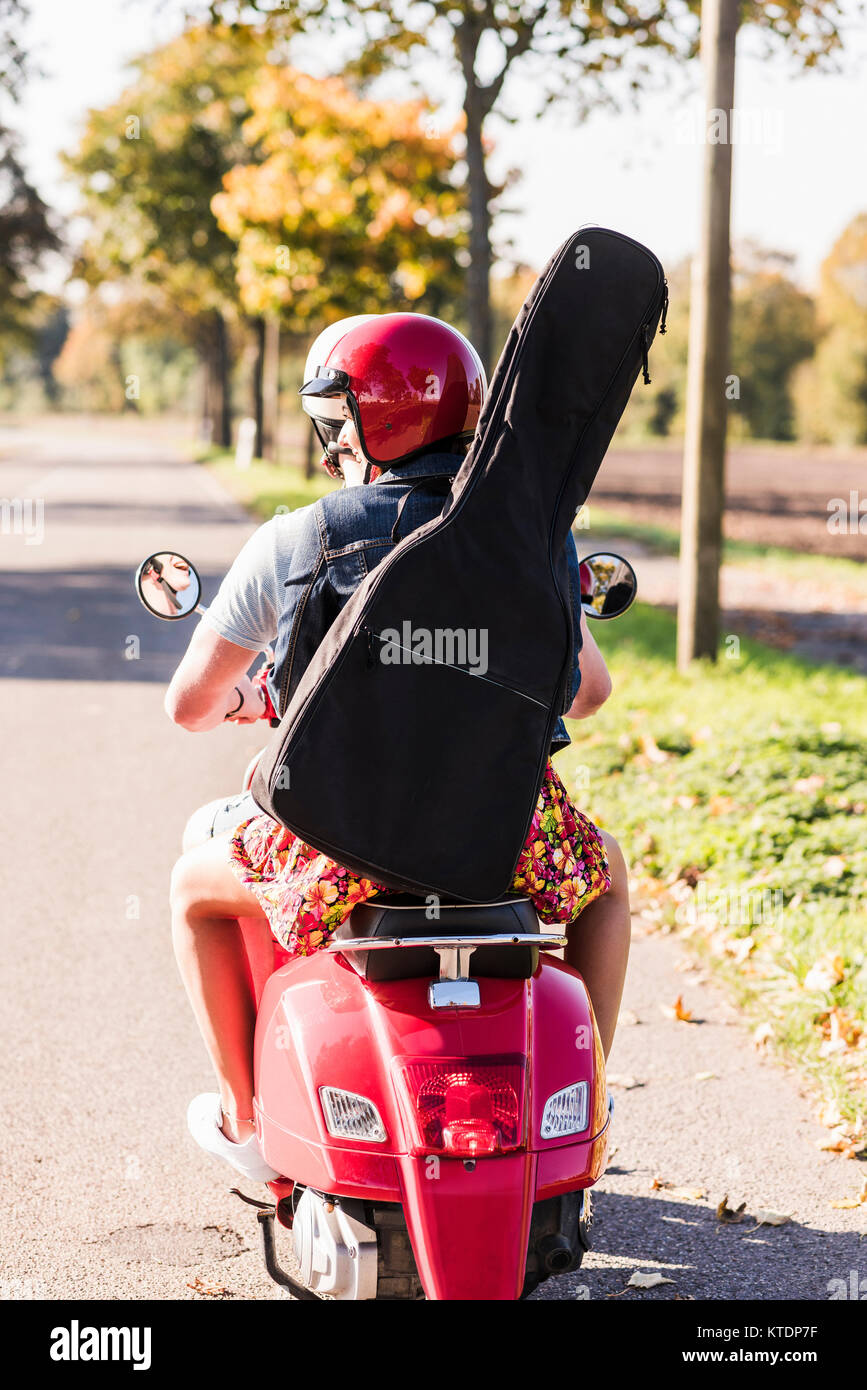 Jeune couple riding scooter avec guitare sac sur le dos Banque D'Images