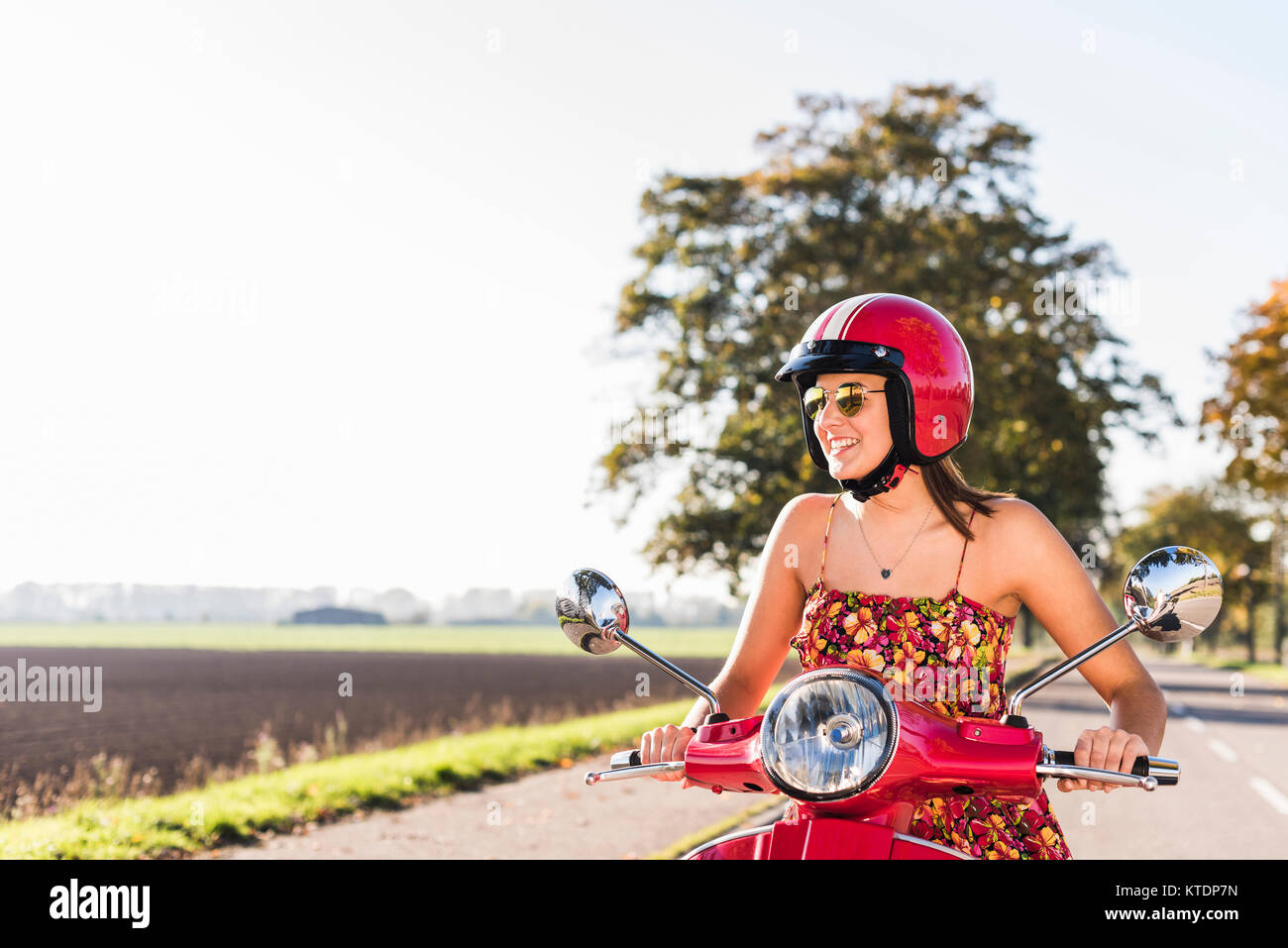 Happy young woman riding scooter on country road Banque D'Images
