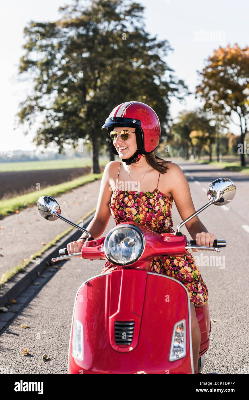 Happy young woman riding scooter on country road Banque D'Images