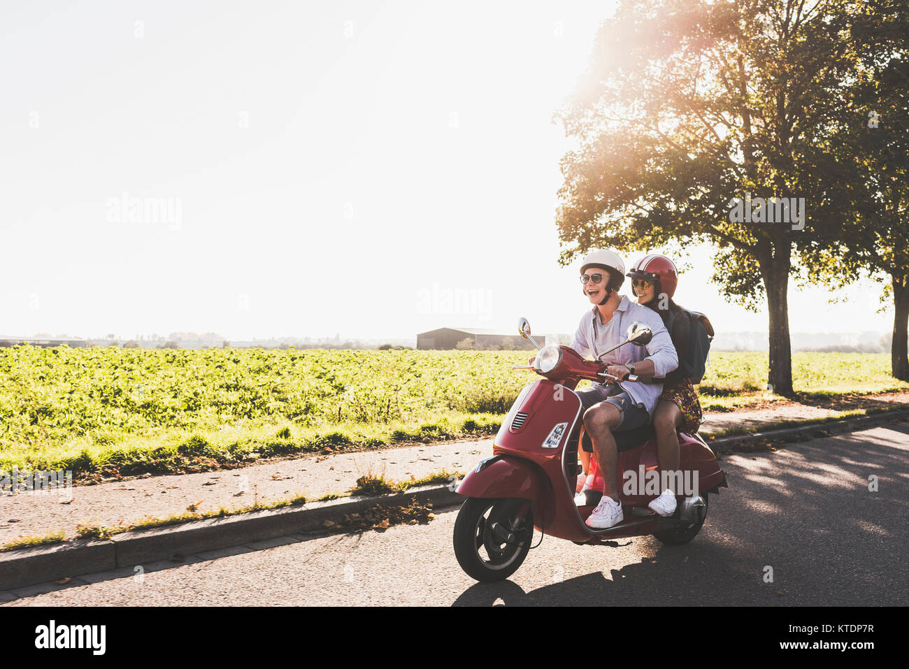 Happy young couple riding scooter on country road Banque D'Images