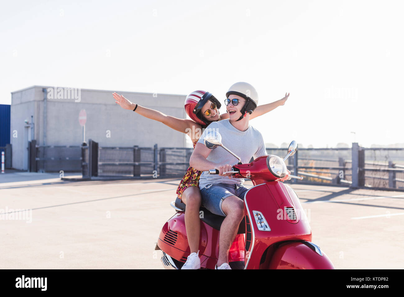 Carefree young couple riding scooter sur niveau parking Banque D'Images