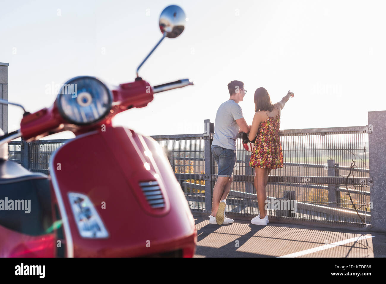 Jeune couple debout sur parking avec scooter en premier plan Banque D'Images