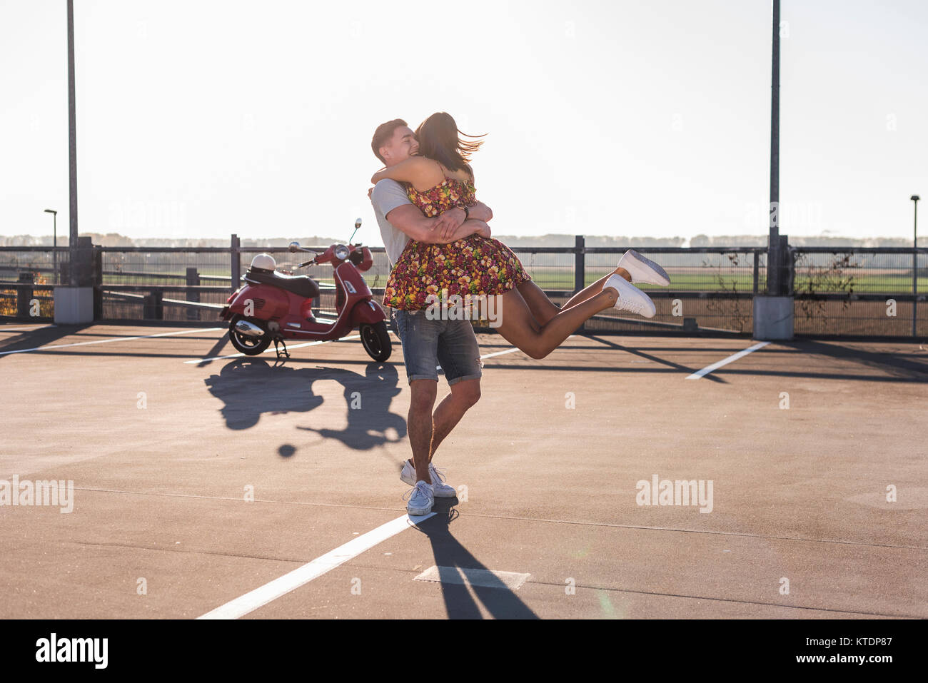 Happy young couple hugging on niveau parking scooter avec en arrière-plan Banque D'Images