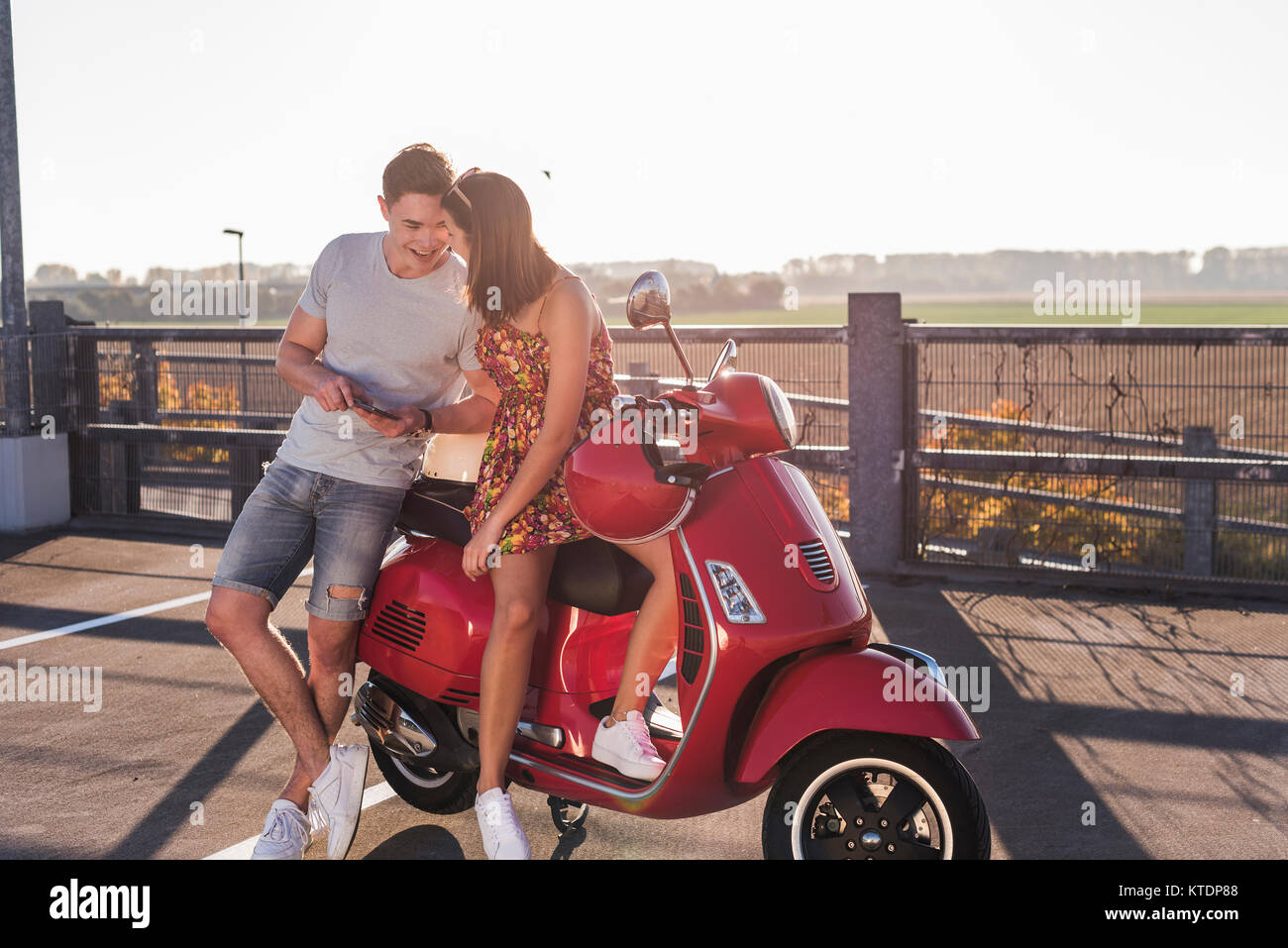 Happy young couple sur parking avec scooter et cell phone Banque D'Images