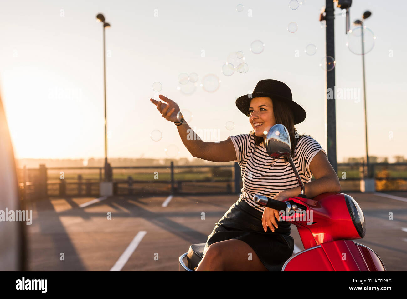 Smiling young woman on motor scooter jouant avec des bulles de savon Banque D'Images