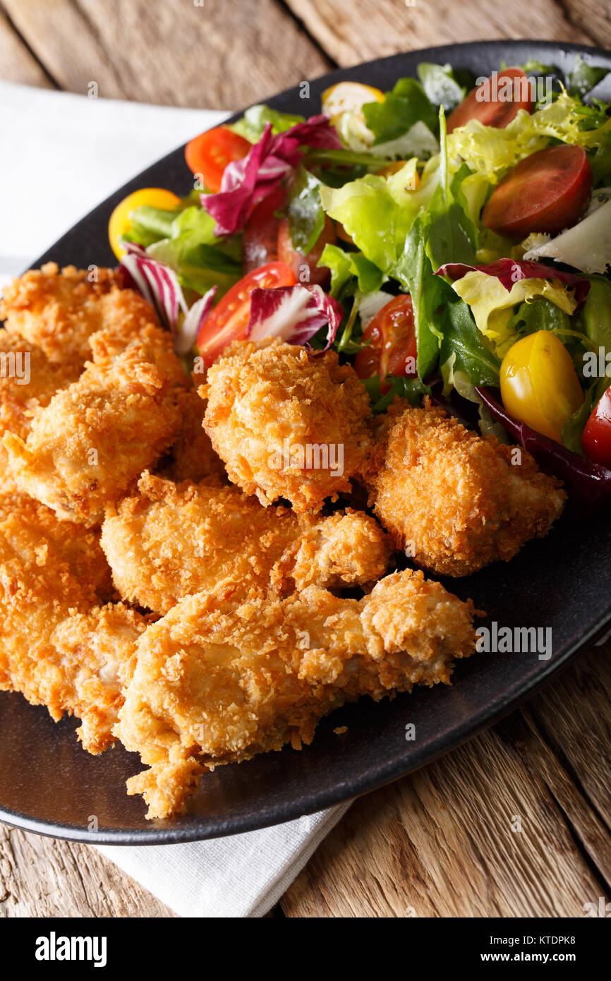 Ailes de poulet pané frit dans une salade de légumes frais et de close-up sur une plaque sur une table verticale. Banque D'Images