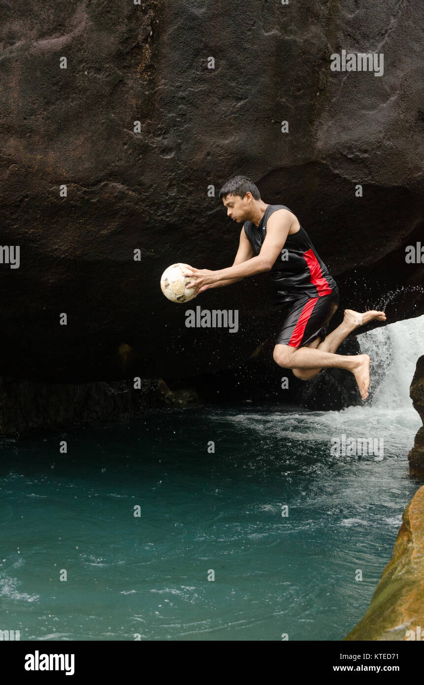 Jeune adulte Jeune Indien l'air, sauter dans l'eau de piscine bleue, tenant une balle sur un Nagarmadi Chendia, chutes d'eau, Karnataka, Inde. Banque D'Images