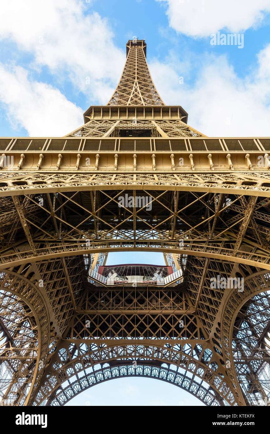 Vue de dessous de la Tour Eiffel, montrant sa structure métallique lacy et marron sous un ciel bleu avec des nuages blancs. Banque D'Images