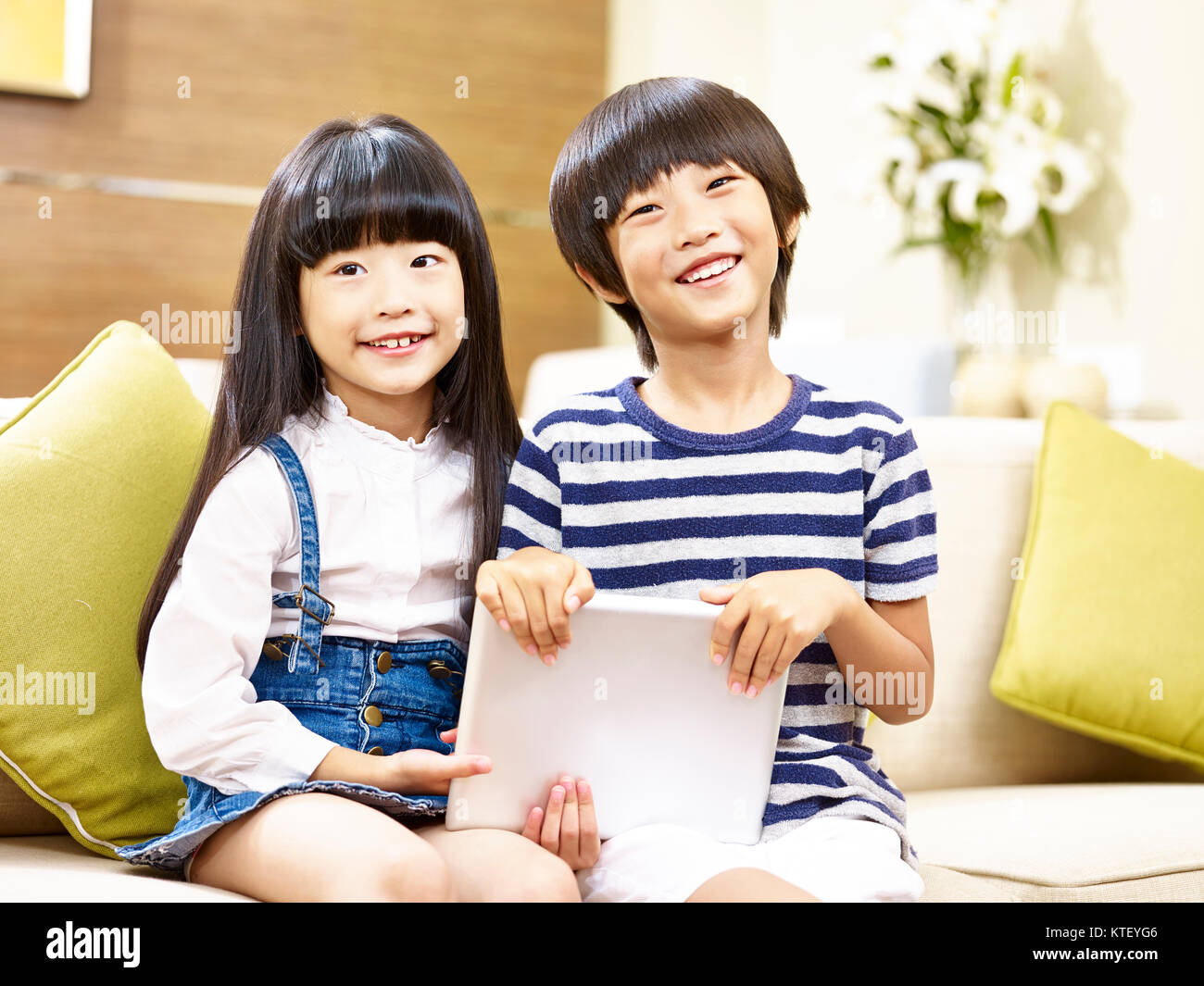 Deux enfants asiatiques mignon petit garçon et petite fille assise sur la table holding digital tablet smiling at camera Banque D'Images