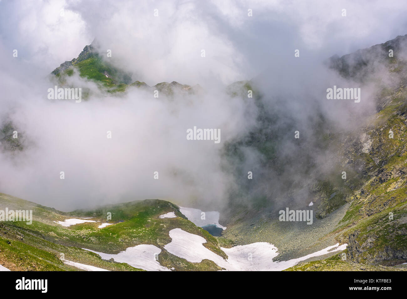 La formation de nuages dans les montagnes de haute altitude. phénomène naturel spectaculaire en été. temps magnifique arrière-plan de collines avec de l'herbe et la neige Banque D'Images